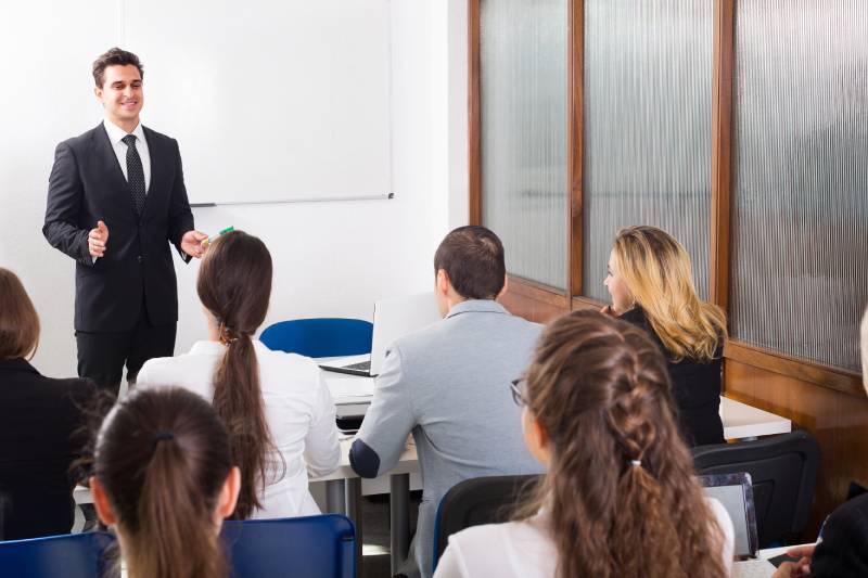 A group of people attending a training having a one to one discussion with the trainer standing before them.